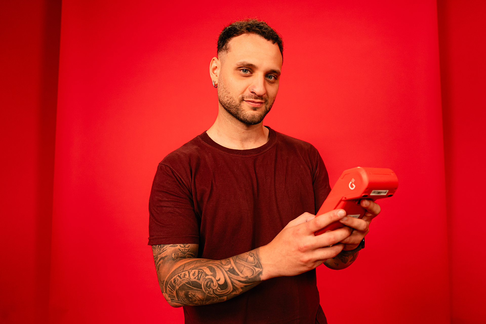 Persona sosteniendo una terminal de cobro roja frente a un fondo rojo.